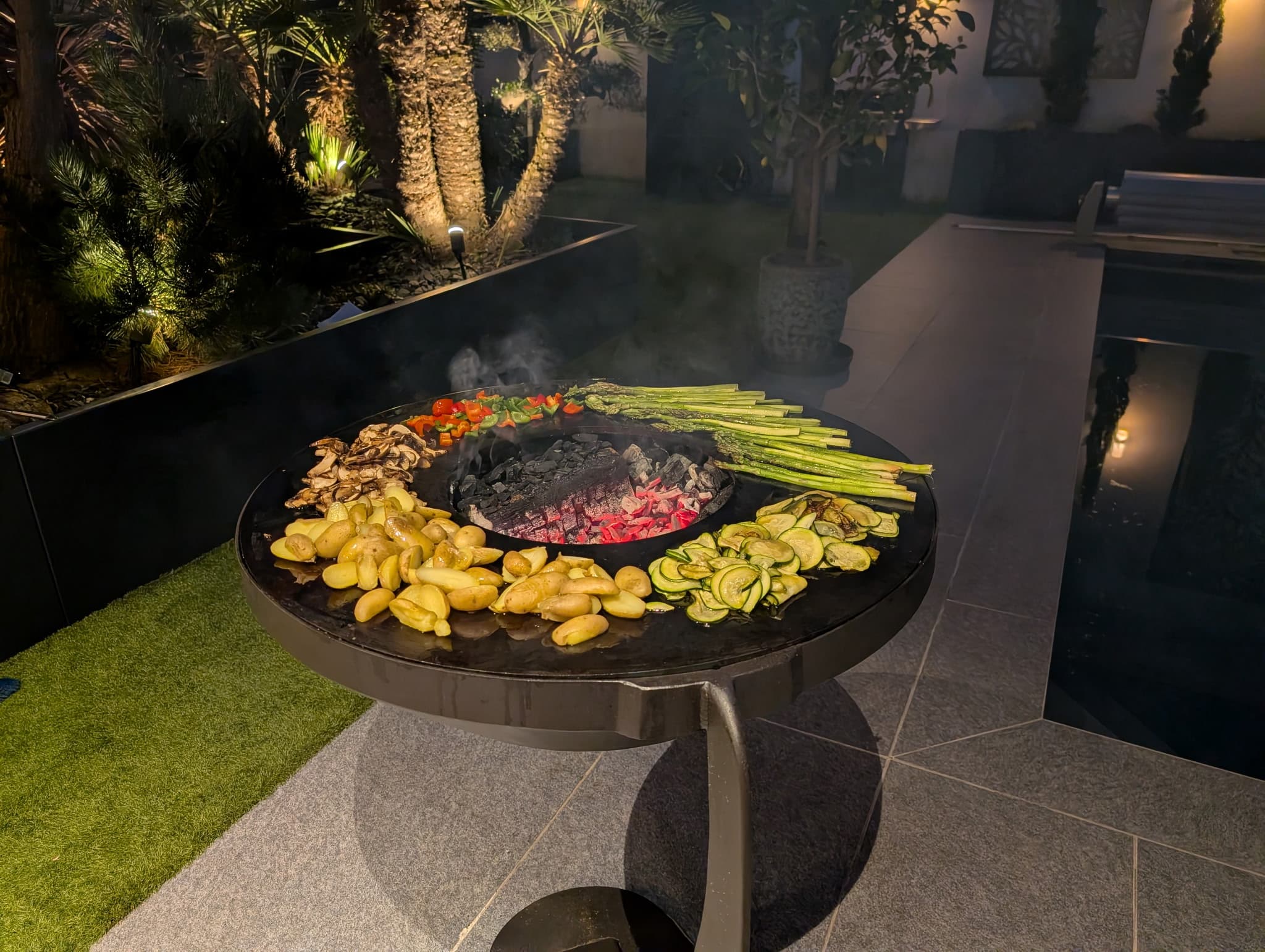 Brasero corten en mode plancha avec légumes grillés en cuisson, ambiance nocturne