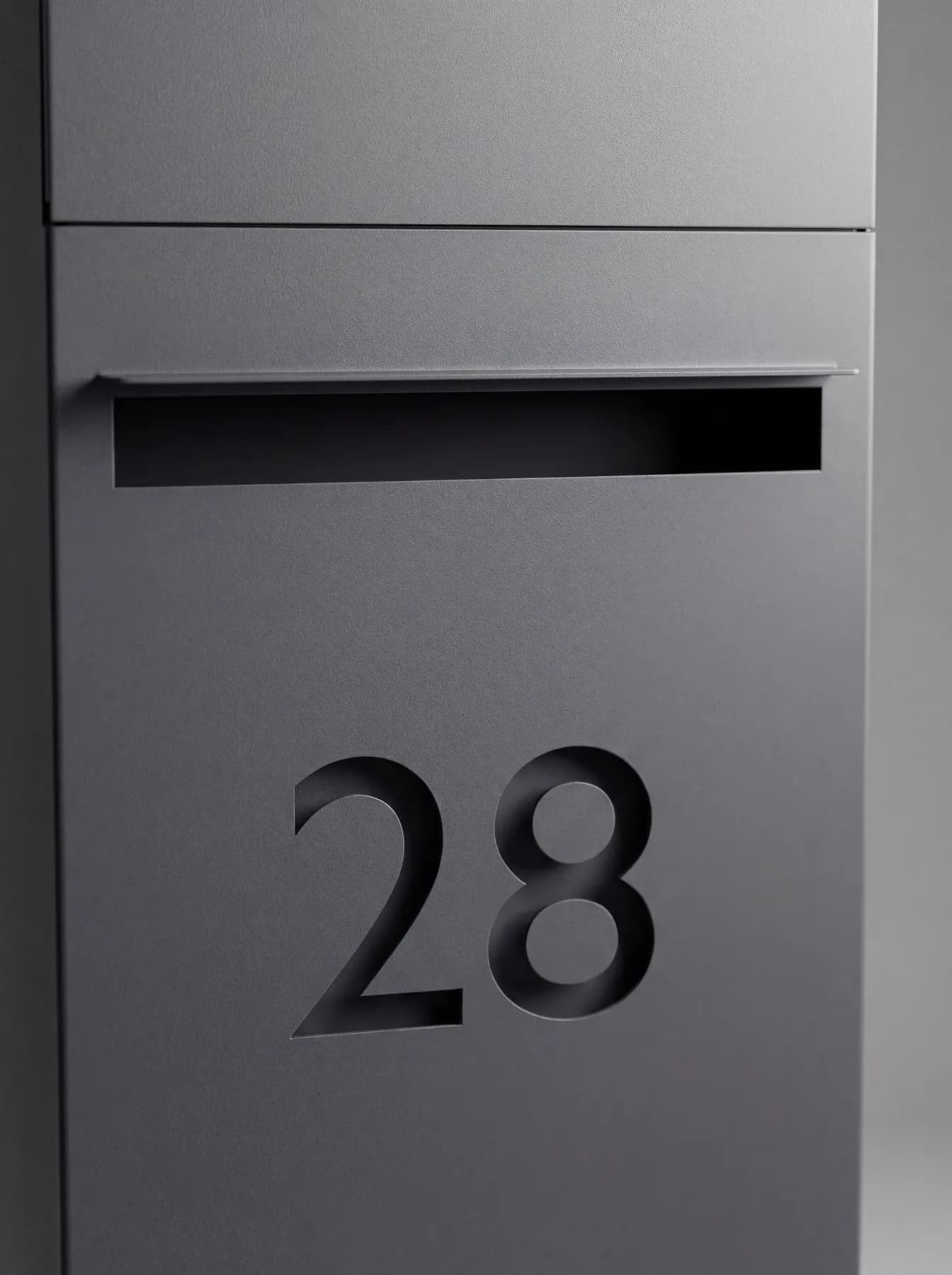 Fente à lettres avec sa casquette et numéro de rue découpé au laser juste dessous, en façade d'une colonne anthracite
