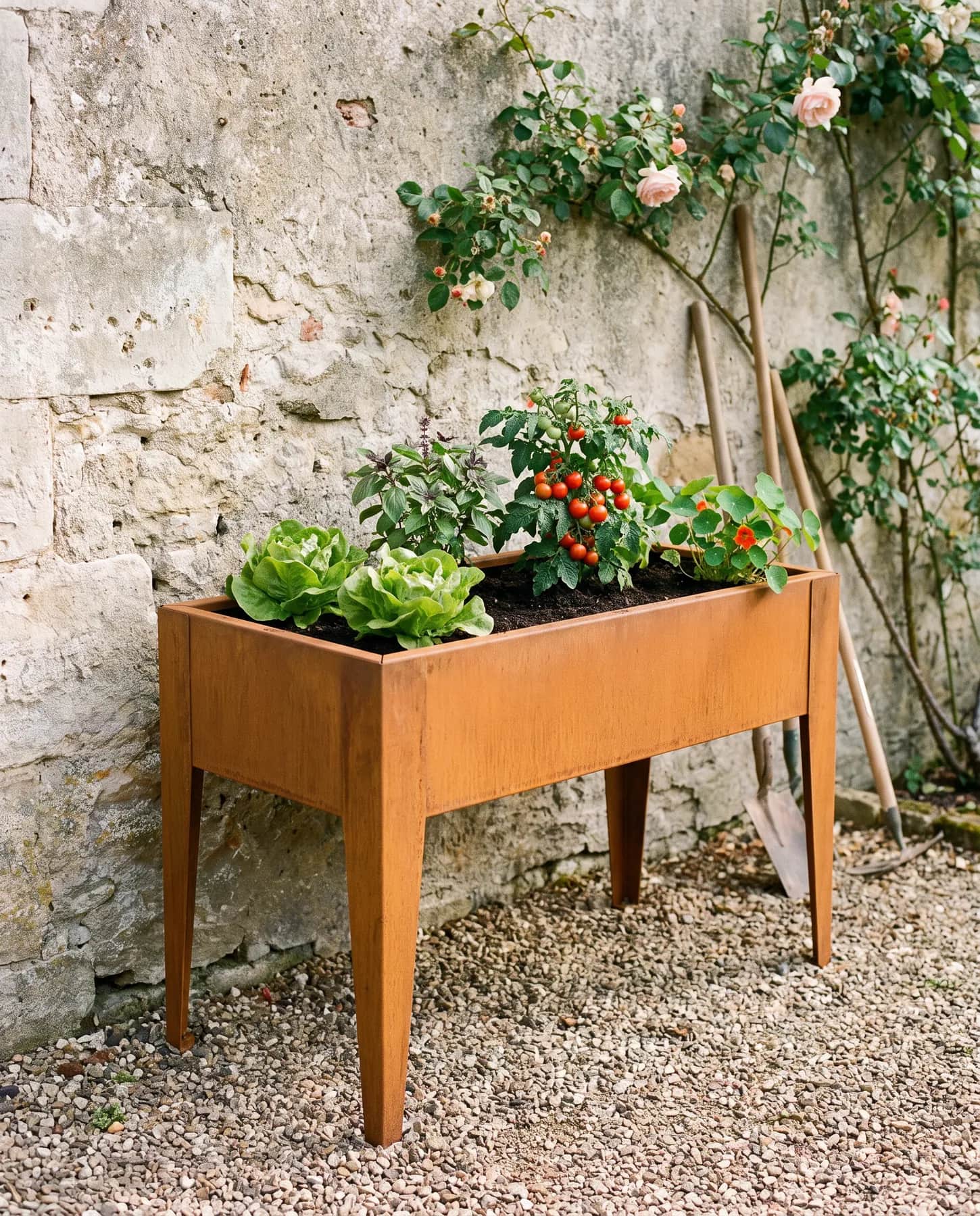 Carré potager sur pieds en acier corten 100 × 50 cm contre un mur de pierre dans un jardin de campagne